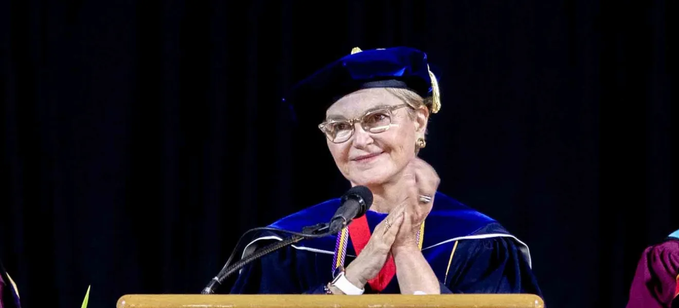 woman in graduation robe speaking at podium