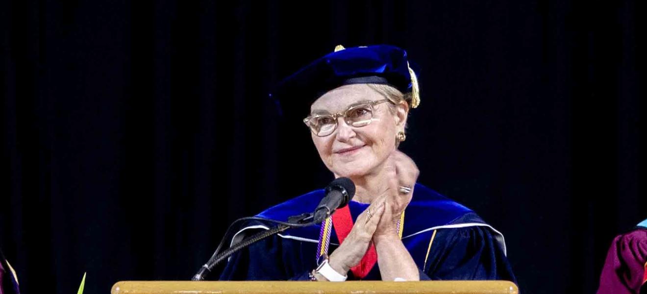 woman in graduation robe speaking at podium