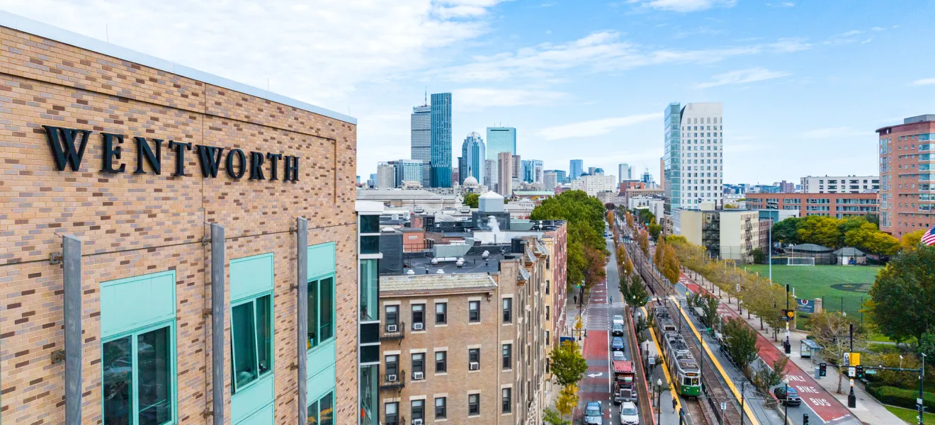 A building on Wentworth's campus with the "Wentworth" name on the side taken by a drone with the city of Boston in the background