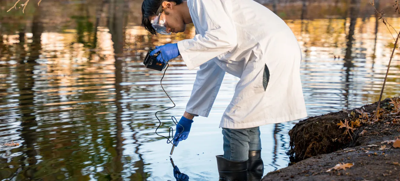 A male student uses a handheld instrument to test a body of water in Boston.