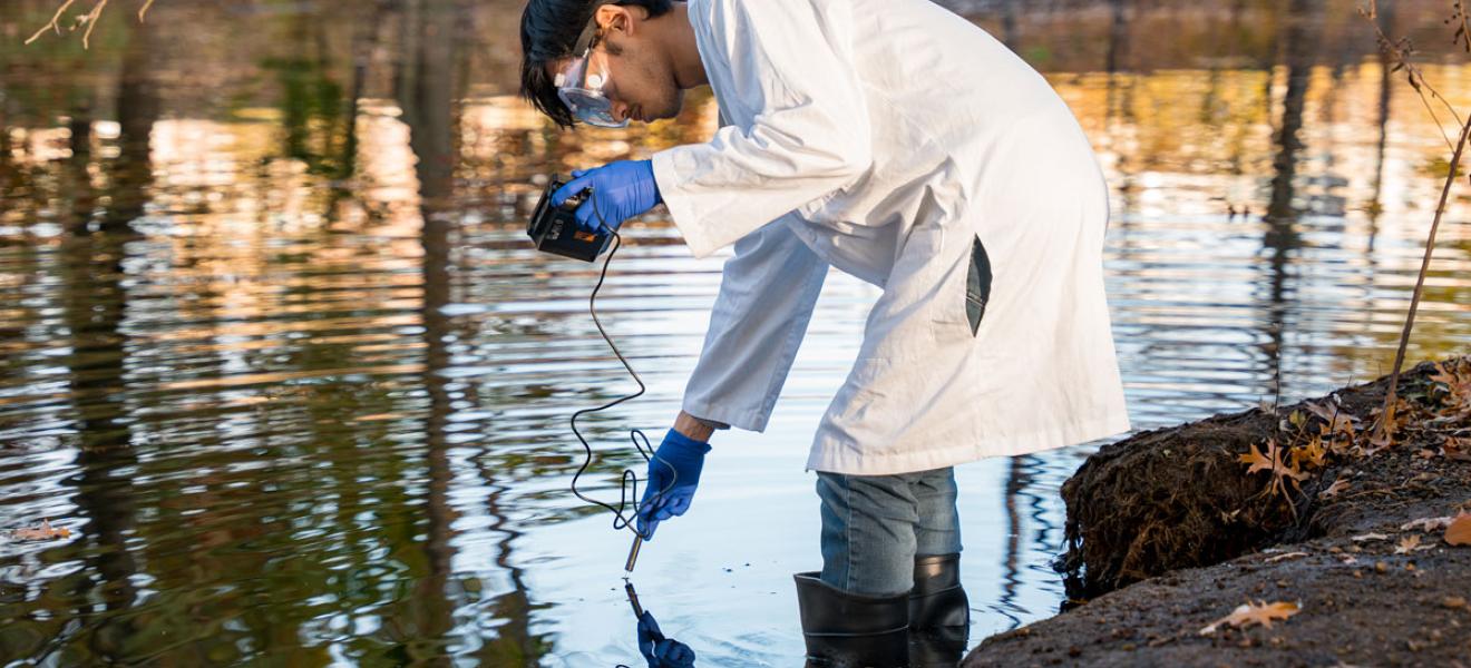 A male student uses a handheld instrument to test a body of water in Boston.