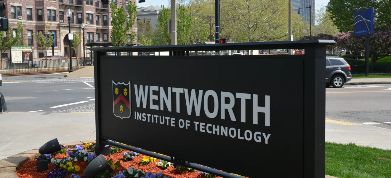 a wentworth sign surrounded by plants with city buildings in the background