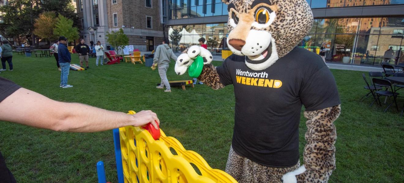 Ruggles the leopard campus mascot plays connect four with participants on the quad during Wentworth Weekend