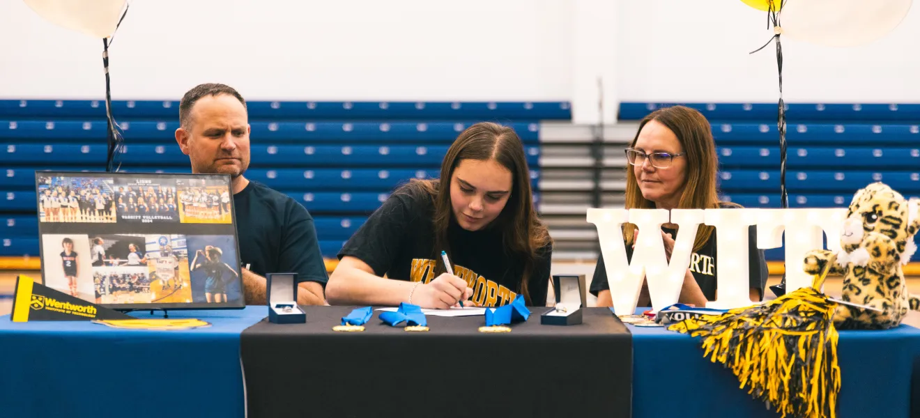 a student signs a piece of paper next to her family