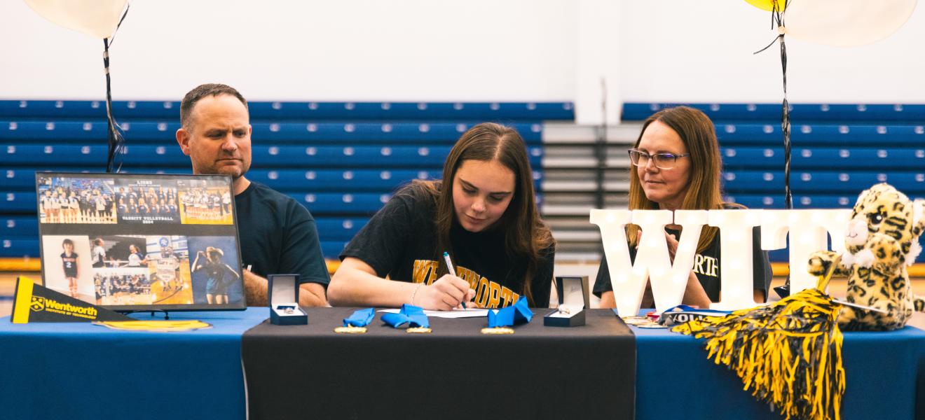 a student signs a piece of paper next to her family