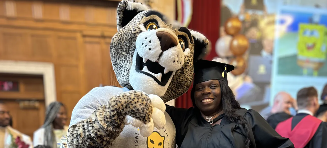 a woman in a graduation robe poses with a leopard mascot