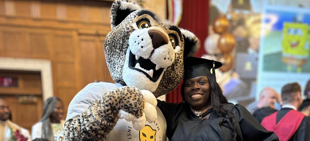 a woman in a graduation robe poses with a leopard mascot