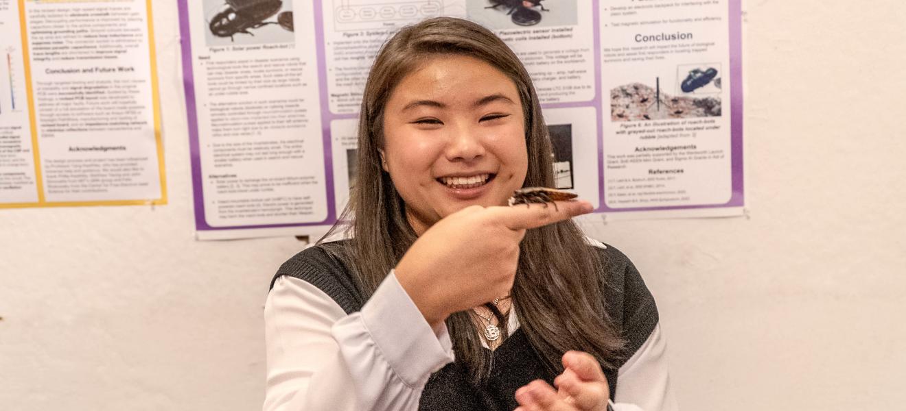 a woman holds up a cockroach fitted with a sensor