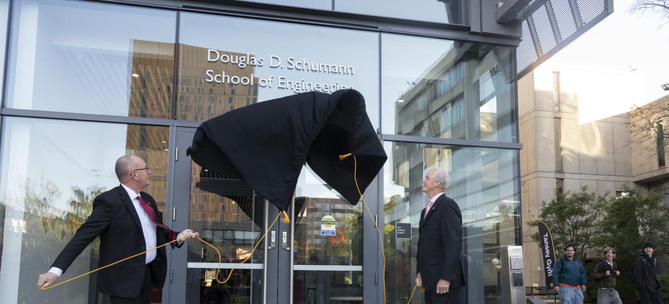 two men remove a covering on a building to reveal a new sign