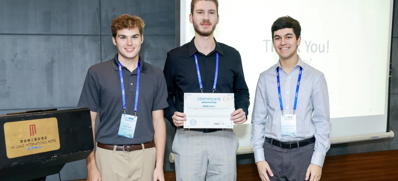 three students stand while one holds a certificate