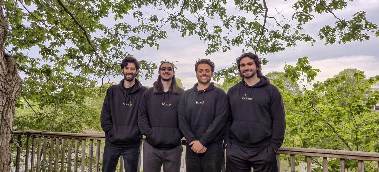 a group of four people pose in black sweatshirts in front of trees