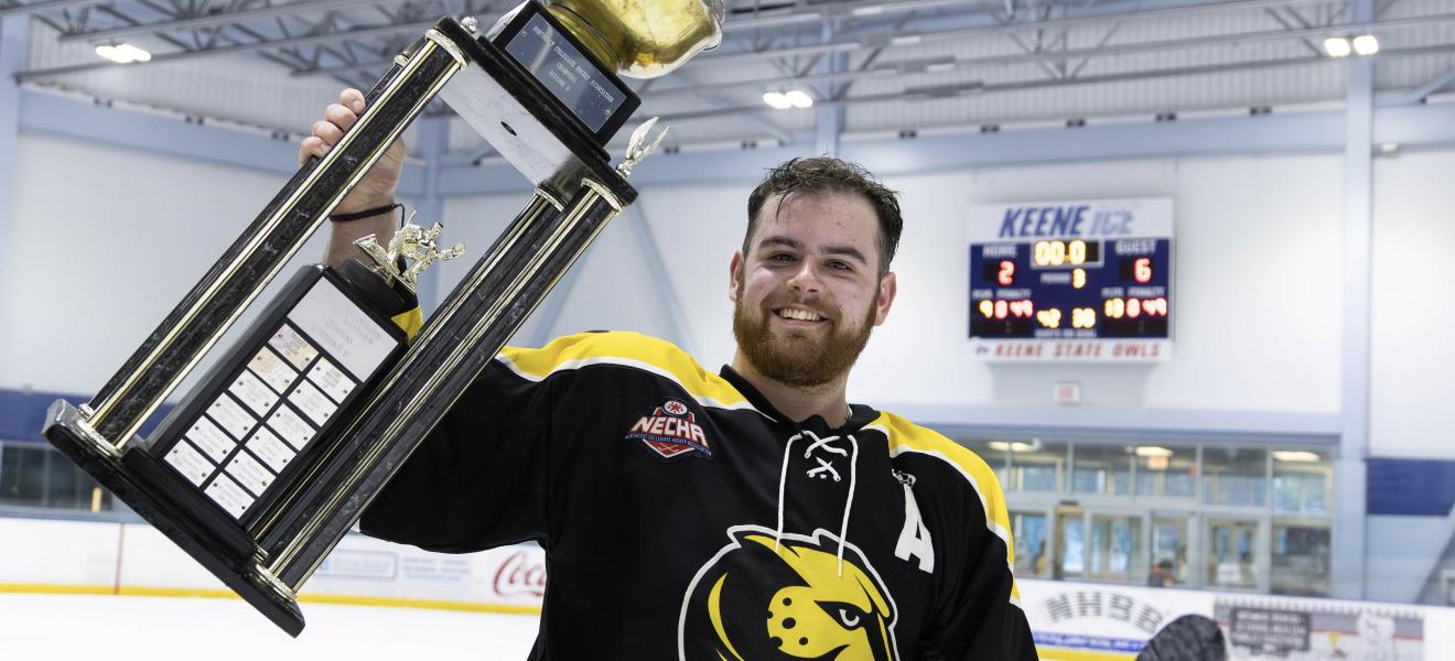 a man in a hockey uniform holds up a trophy