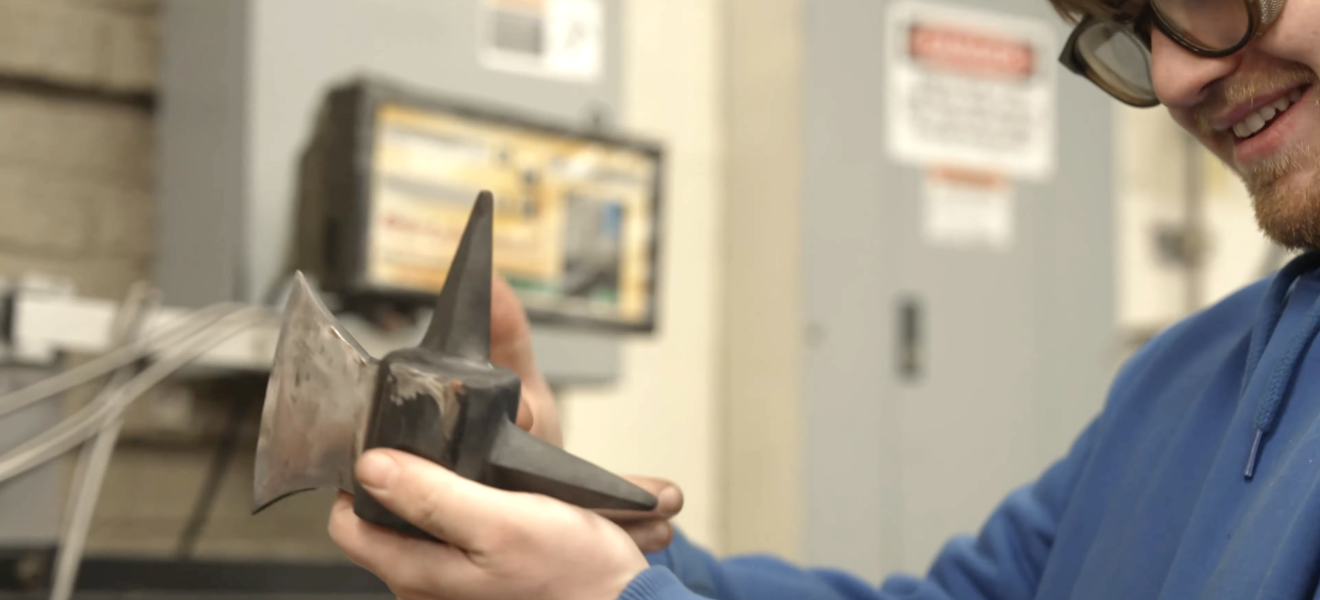 a student holds up a steel axe part