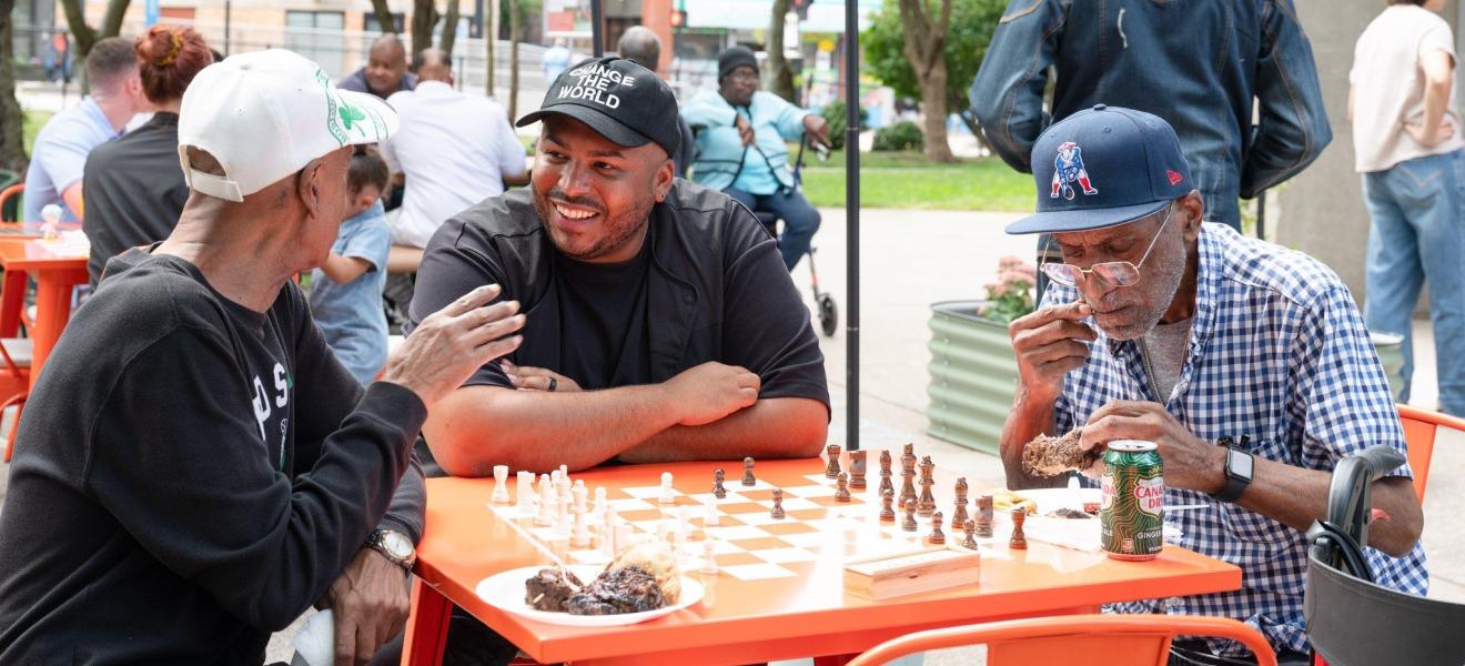 three men having a chat over a chess board outdoors