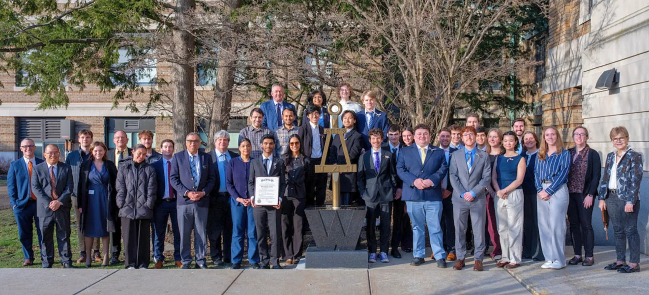 a large group of people pose in front of a statue on a college campus