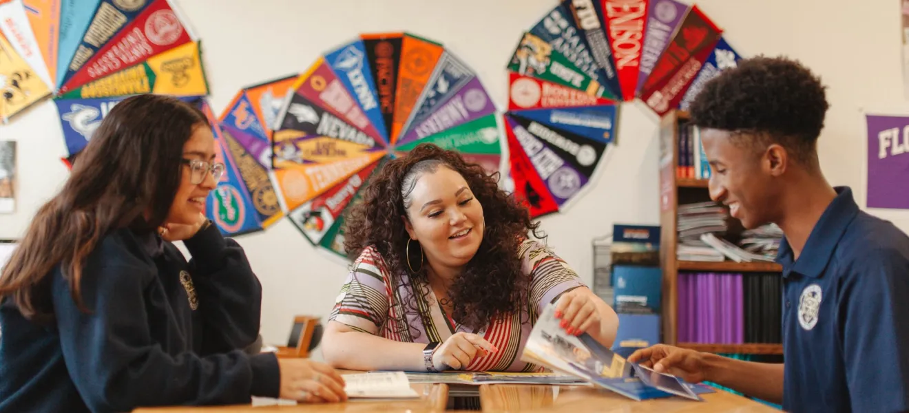 three people sit at a table with college banners on the walls behind them