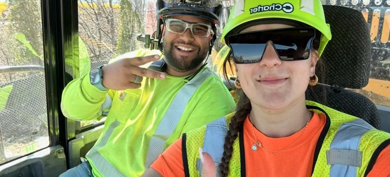 two people in hard hats and vests witting in an excavator