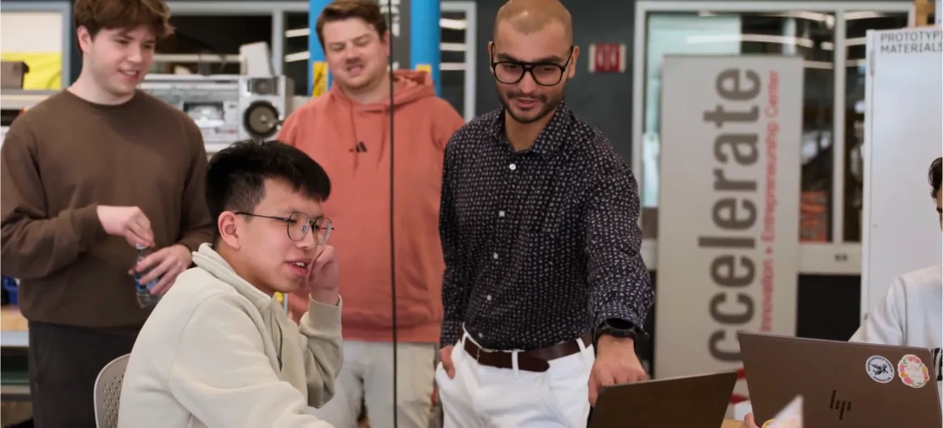 students and a professor look at a computer screen together