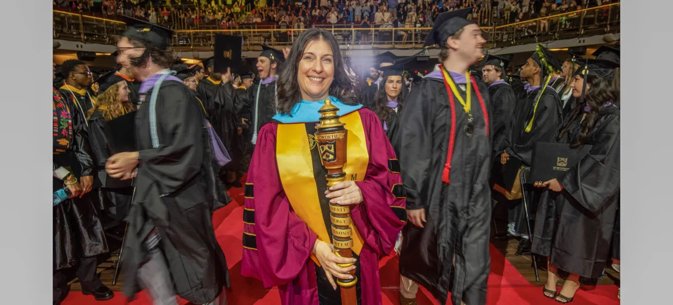 a woman in a graduation robe is surrounded by students in graduation robes in an indoor arena