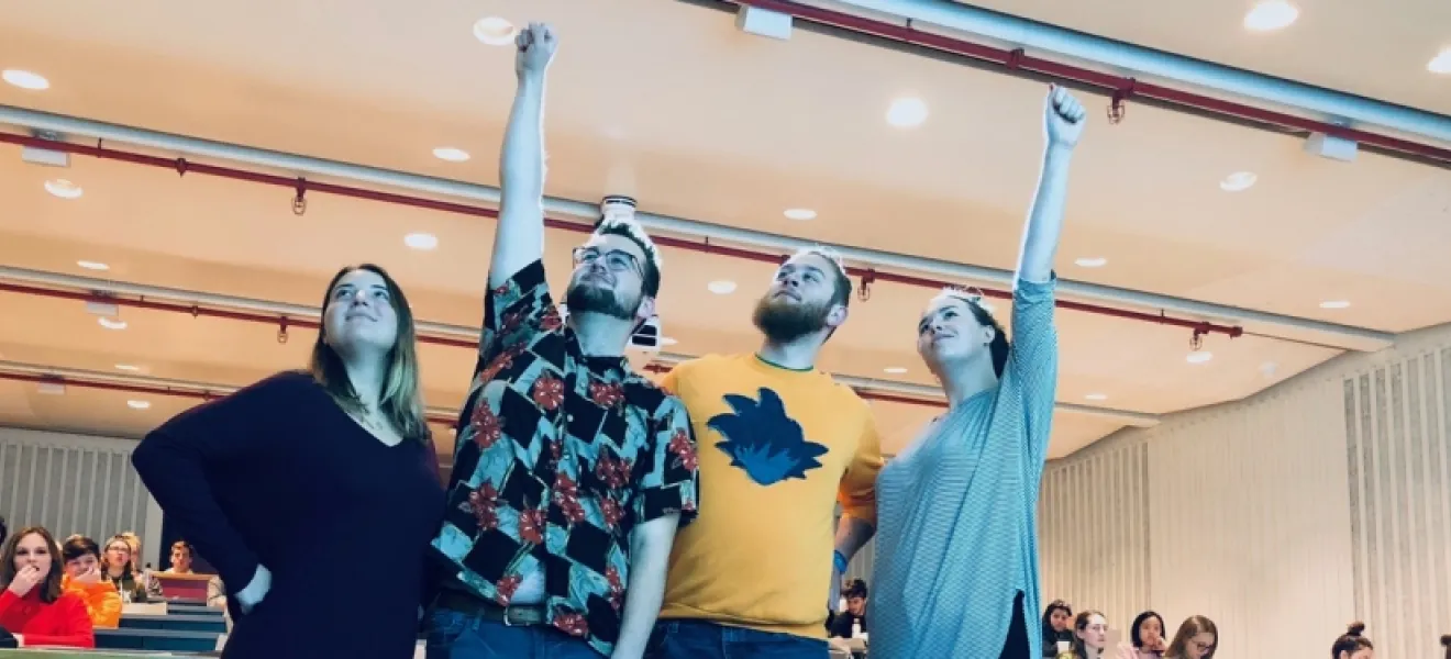 four students standing with their arms raised triumphantly in the air