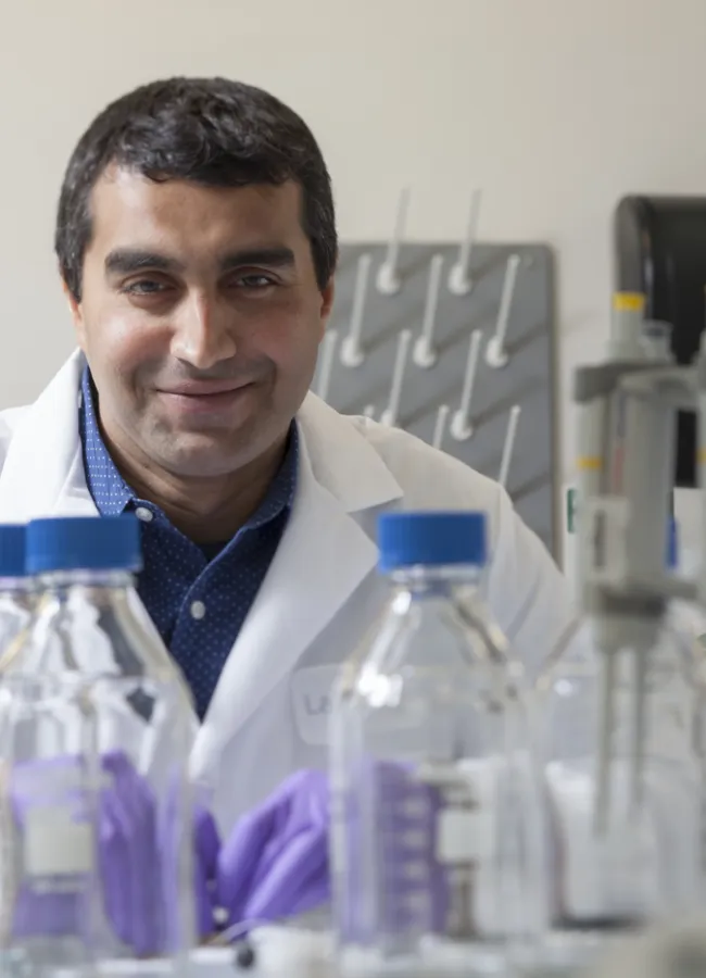 Salil Desai smiles behind a row of beakers