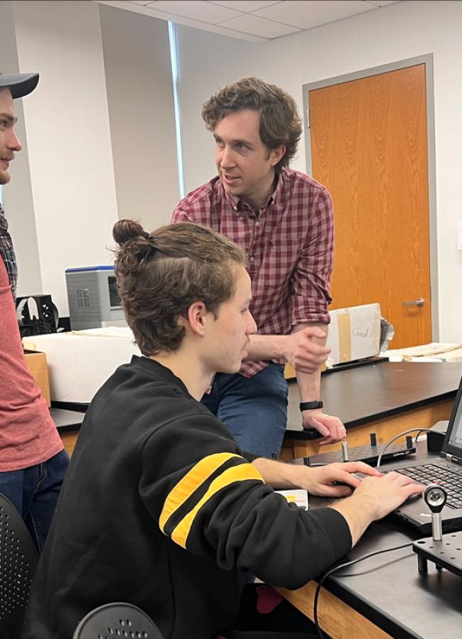 Andrew Seredinski works with two students on a computer in the lab
