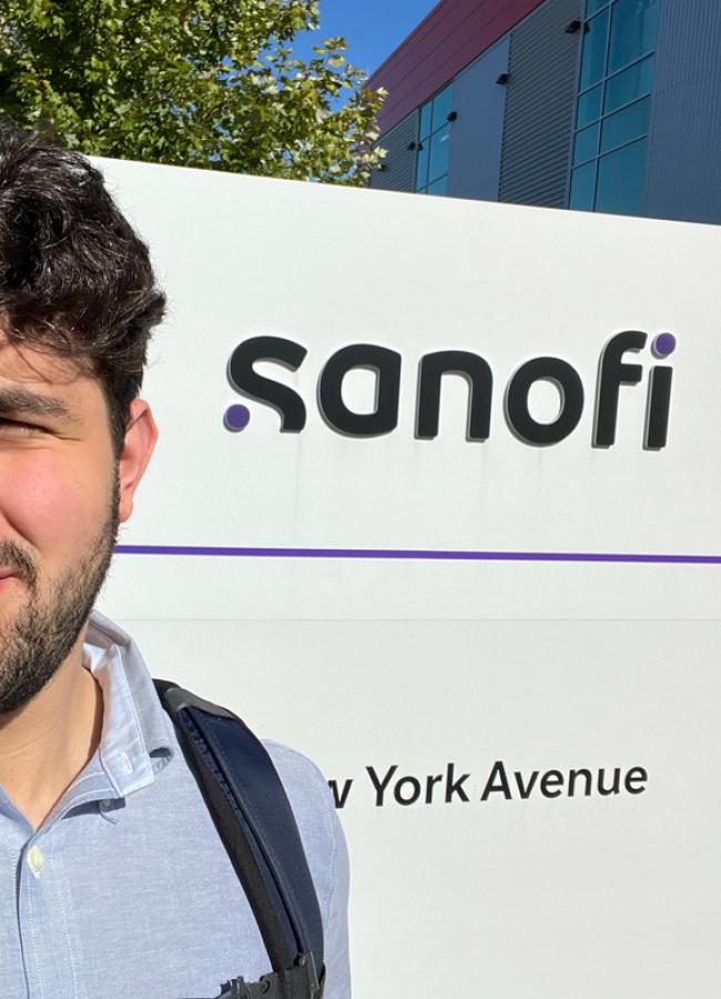 Mustafa Abdulnabi stands in front of the Sanofi company sign