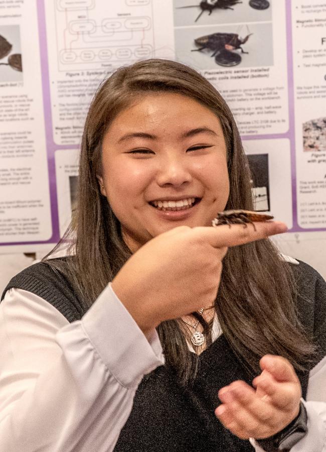 a woman holds up a cockroach fitted with a sensor